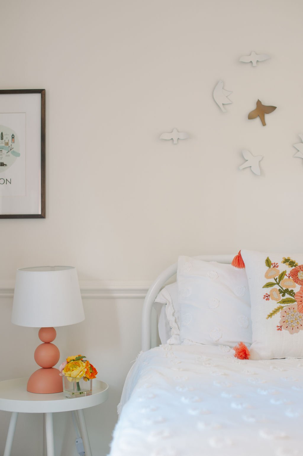 Little Girl's room with white metal headboard, white comforter, floral pillow, bird art, coral sculptural table lamp, round nightstand