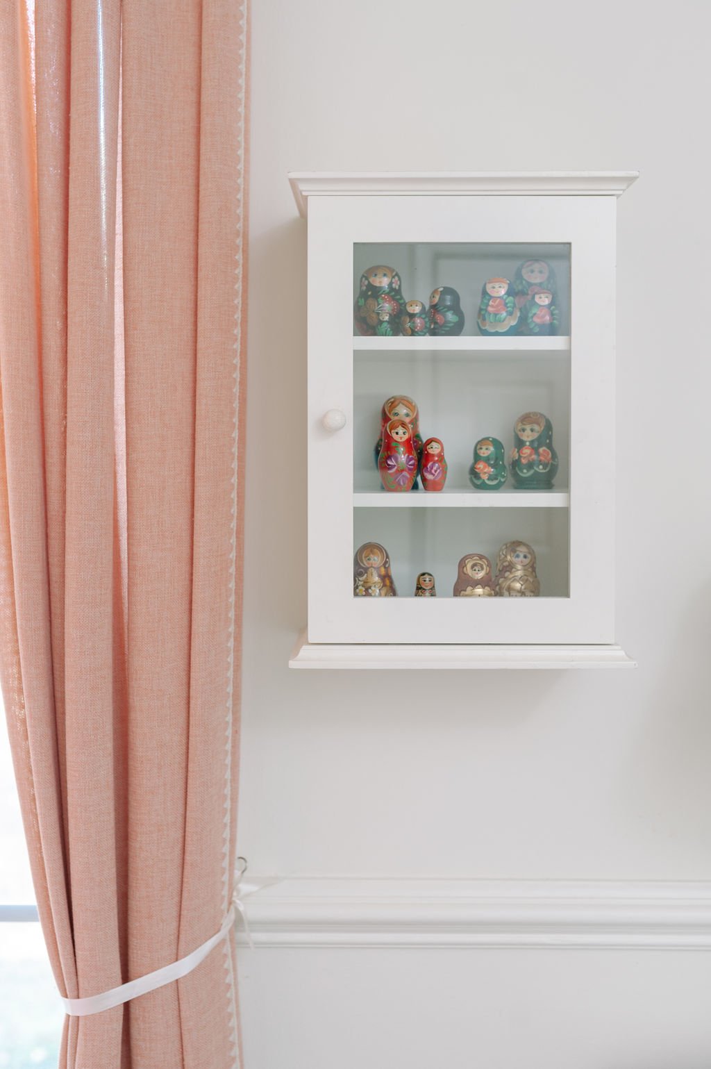 White curio cabinet with Russian Matryoshka dolls, coral curtains